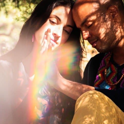 German Virguez and Lupita Castro embracing in a forest, illuminated by a rainbow light flare